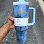 ماگ استنلی مدل Quencher Tumbler H2.0 کنار لپ‌تاپ روی میز کار