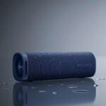 اسپیکر Xiaomi Sound Outdoor 30W قرارگرفته روی میز کنار گوشی